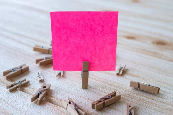 Piece Of Blank Square Note Surrounded By Laundry Clips Showing New Meaning. Empty Sticky Paper Clipped Upright Placed On Top Of Wooden Table Displaying Fresh Idea.