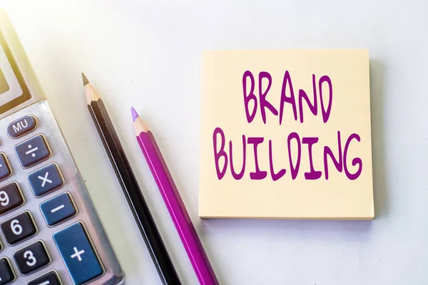 Scrittura visualizzazione testo Brand Building. Attività fotografiche concettuali associate all'istituzione e alla promozione di un marchio Plain Spiral Notebook con penna accanto a calcolatrice e monete sul tavolo. — Foto Stock