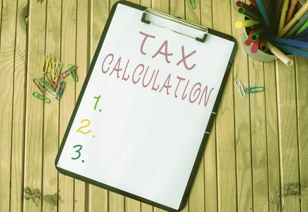 税額計算を示すテキスト記号 政府に支払う金額の評価に書かれた単語テーブルの上に置かれたホルダーにペンのスタックを持つプレーンオフィスクリップボード — ストック写真