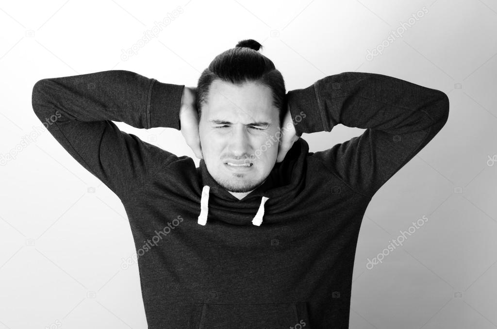 Portrait young annoyed, unhappy, stressed man covering his ears, looking up, to say, stop making loud noise, giving me headache isolated on grey background with copy space. Negative emotion reaction
