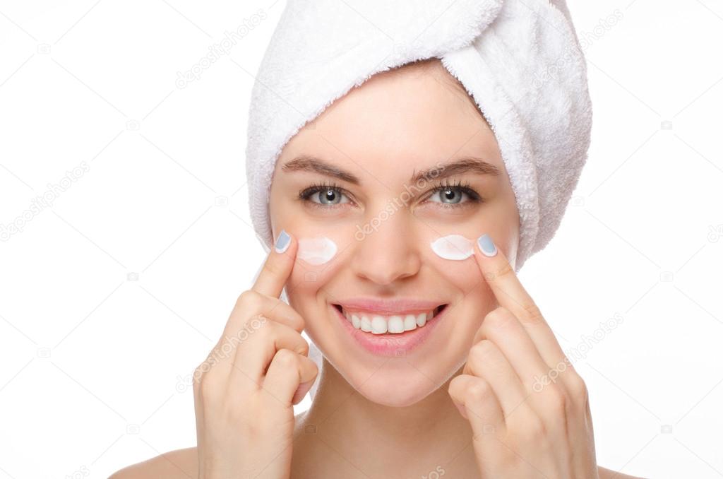 Beautiful young woman applying a creme on her face isolated on white background