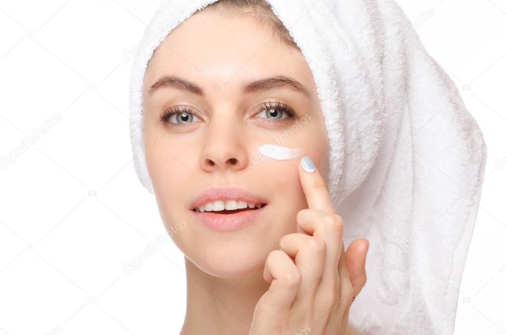 Skin care woman putting face cream touching under eyes. Facial beauty closeup of beautiful female model on white background.