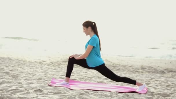 Giovane donna che fa esercizio di yoga sulla spiaggia di sabbia estiva all'alba — Video Stock