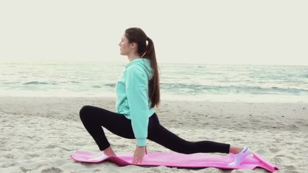 Young woman practicing yoga on the beach near the sea — Stock Video