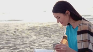 Genç kadın okuma termos sıcak çay veya kahve içme plaj üzerine bir kitap