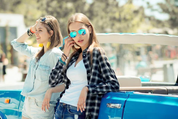 Senhoras bonitas em óculos de sol posando perto do carro vintage cabriole — Fotografia de Stock