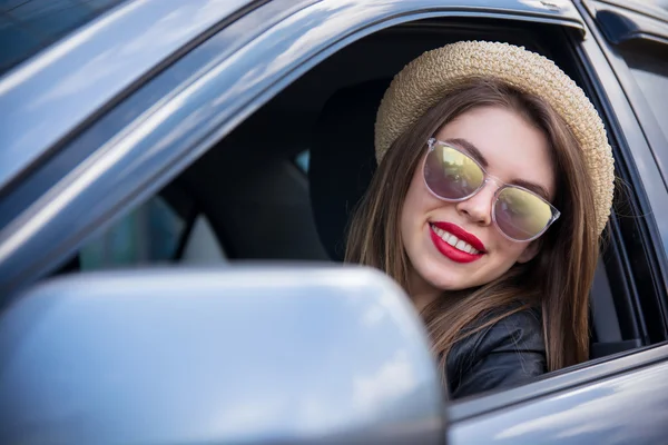 Счастливая женщина в летней шляпе и солнцезащитных очках за рулем автомобиля на улице — стоковое фото
