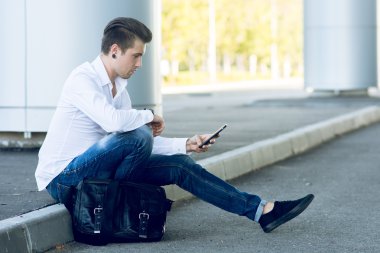 road yakınındaki otururken Smartphone kullanarak yakışıklı genç