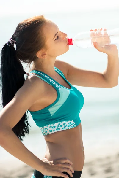 Фитнес-женщина пьет воду после бега на пляже — стоковое фото
