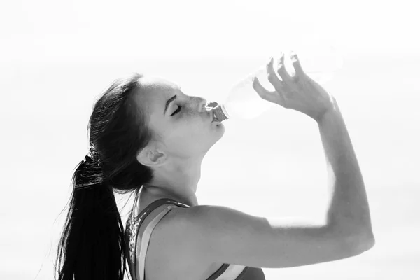 Fitness woman drinking water after running at beach — Stock Photo, Image