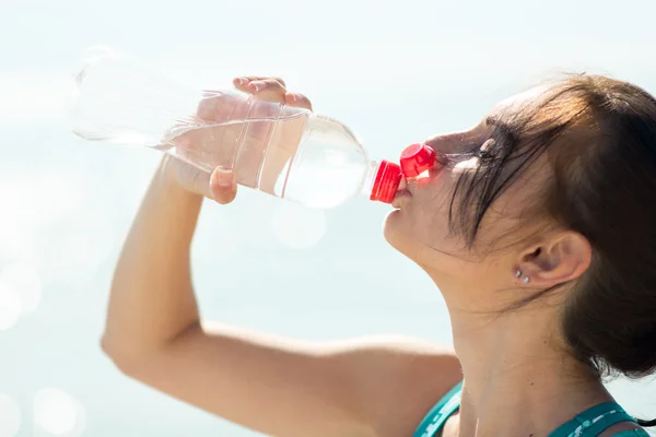 Fitness woman drinking water after running at beach — Stock Photo, Image