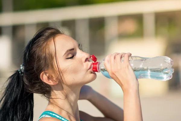 Фитнес-женщина пьет воду после бега на пляже — стоковое фото