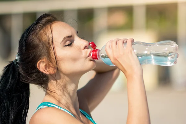 Фитнес-женщина пьет воду после бега на пляже — стоковое фото
