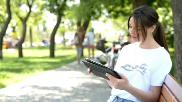 Jeune femme avec tablette sur le banc dans le parc d'été — Video