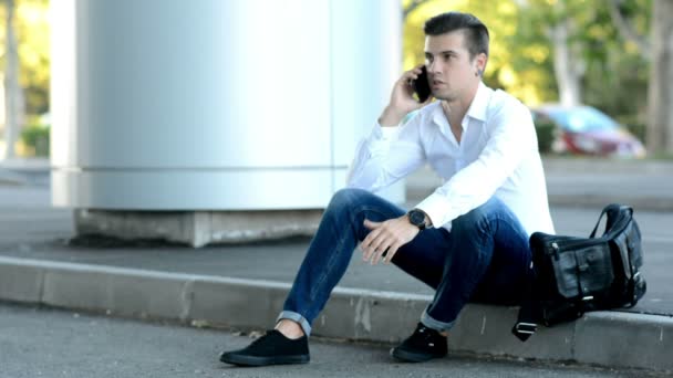 Mann sitzt auf der Straße und spricht mit Smartphone — Stockvideo