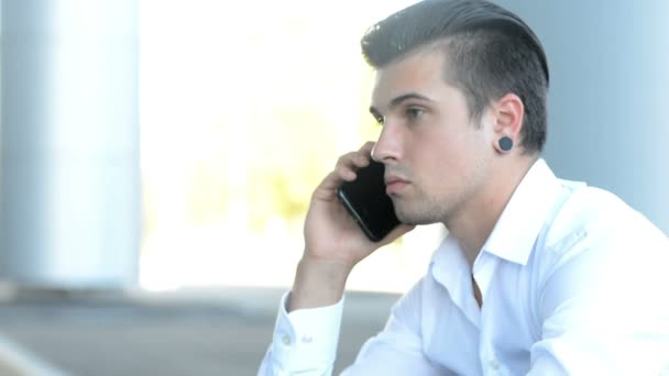 Молодой человек разговаривает по телефону на улице возле вокзала — стоковое видео
