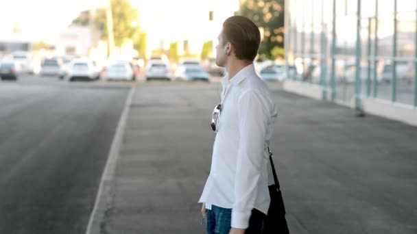 Hombre camina y escuchar música de auriculares cerca del centro de negocios, sacudiendo la cabeza — Vídeo de stock