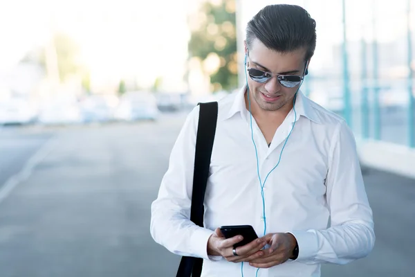 Joven guapo con teléfono inteligente y auriculares escuchar música — Foto de Stock