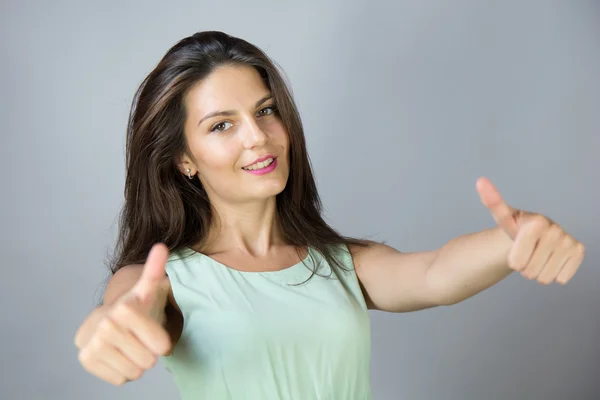 Portret van een jong meisje glimlachend brunette met duimen omhoog — Stockfoto