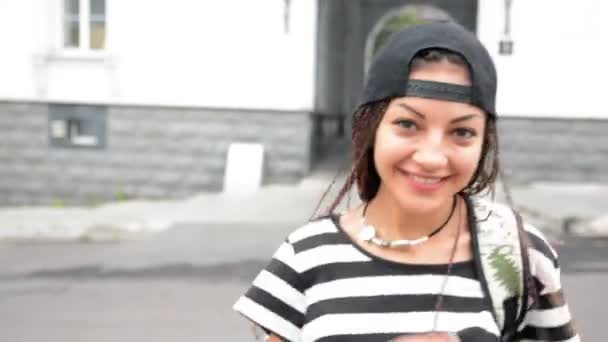 Young woman with dreadlocks put on the cap and walk by street — Stock Video