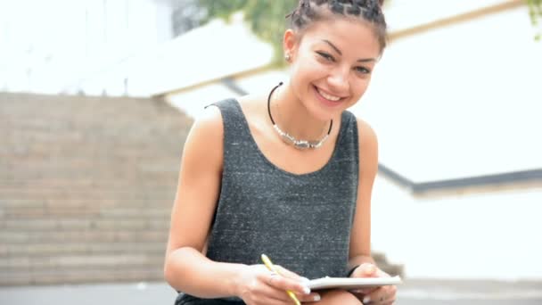 Woman sitting on the stair and write down notes in the notebook — Stock Video