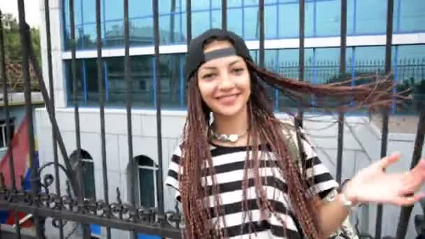 Młoda kobieta z dredy i cap idzie przez ulicę — Wideo stockowe
