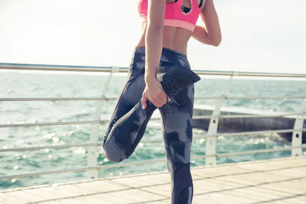Sportos fiatal nő az nyúlik a lábát a strandon — Stock Fotó