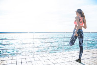 Atletik genç kadın bacağı sahilde germe