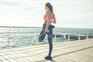 Atletik genç kadın bacağı sahilde germe