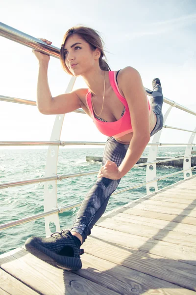 Красивая юная спортсменка, растягивающая ноги на пирсе у моря — стоковое фото