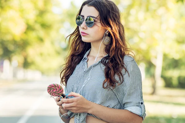 Chica sosteniendo piruleta y escuchando música en los auriculares — Foto de Stock