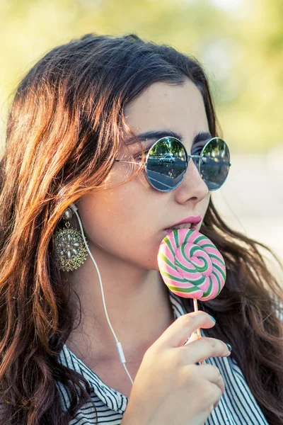 Chica sosteniendo piruleta y escuchando música en los auriculares — Foto de Stock