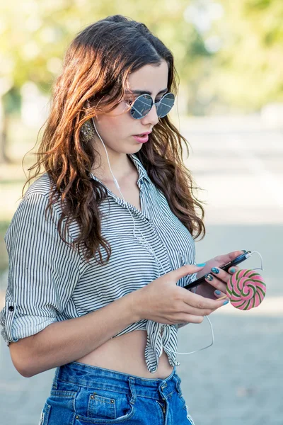 Chica sosteniendo piruleta y escuchando música en los auriculares — Foto de Stock