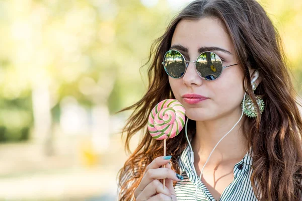 Chica sosteniendo piruleta y escuchando música en los auriculares — Foto de Stock