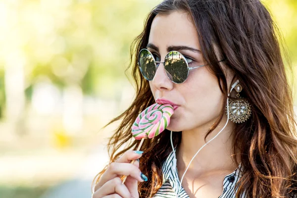 Chica sosteniendo piruleta y escuchando música en los auriculares — Foto de Stock