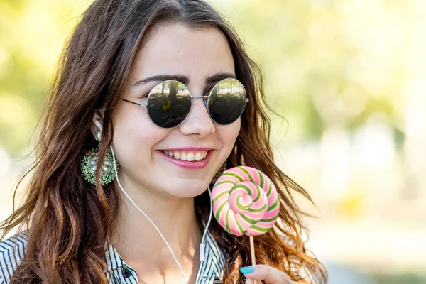 Menina segurando pirulito e ouvir música em fones de ouvido — Fotografia de Stock