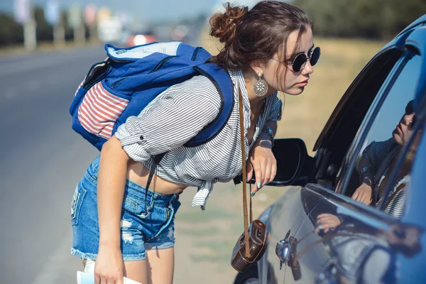 Молодая женщина-автостопщик спрашивает дорогу к водителю — стоковое фото