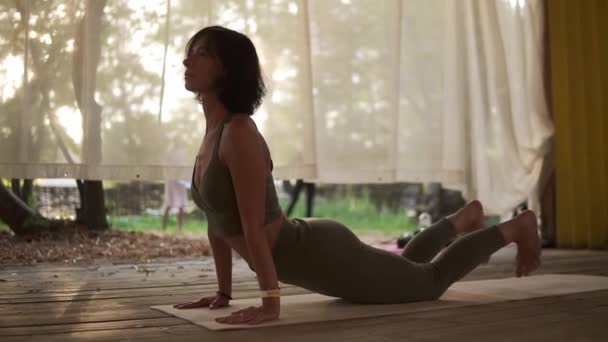 Fit mulher está fazendo ioga em cabana de madeira cheia de luz, a menina executa stands de ioga e elementos — Vídeo de Stock