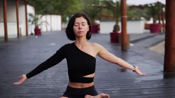 Жінка в чорному, сидячи в лотосі позує медитуючи і дихаючи один на відкритому повітрі — стокове відео