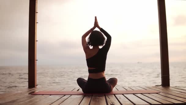 Wanita berlatih yoga dan meregangkan tulang belakang dan tangan duduk di atas tikar di dermaga laut memegang tangan di atas kepala — Stok Video