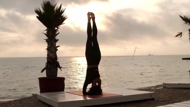 Mulher de pé na cabeça em ioga pose salamba shirshasana ao ar livre, praticando ioga asana na praia em frente ao mar — Vídeo de Stock