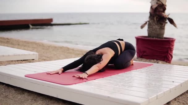 Nő gyakorló jóga és nyújtózkodó gerinc feküdt matrac előtt a tenger reggel — Stock videók