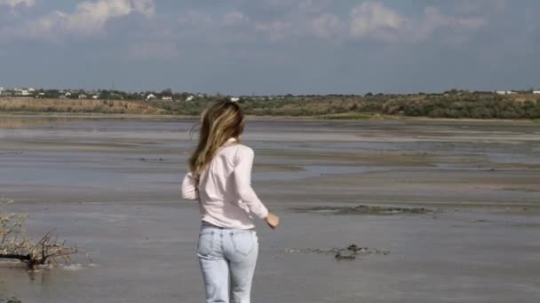 Zeldzaam uitzicht van vrolijke vrouw in casual loopt op zand ondiep van het meer in de zomer — Stockvideo