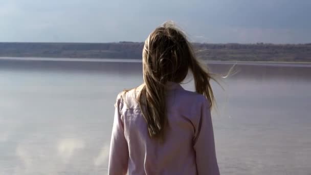 Achteraanzicht van langharige vrouw met uitzicht op rivier met wind waait — Stockvideo