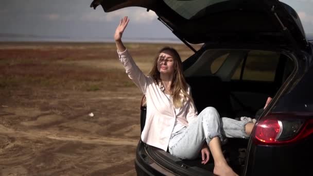 Portrait d'une femme assise dans le coffre de la voiture pieds nus, relaxant et se cachant du soleil doux avec la main — Video