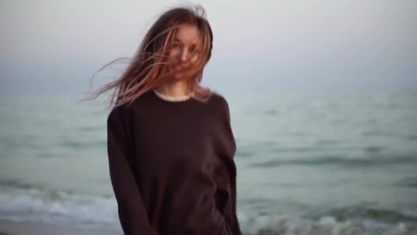 Langharige vrouw loopt gelukkig langs de herfstkust, kijkend naar de camera — Stockvideo