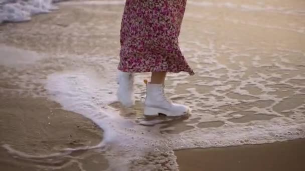 Meisje in elegante kleren loopt langs de kust stappen op schuimige golven — Stockvideo