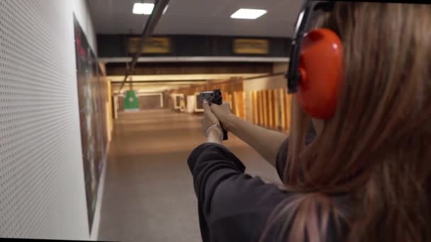 Mulher de cabelos longos em treinamentos de fones de ouvido de proteção na faixa de tiro, visando — Vídeo de Stock