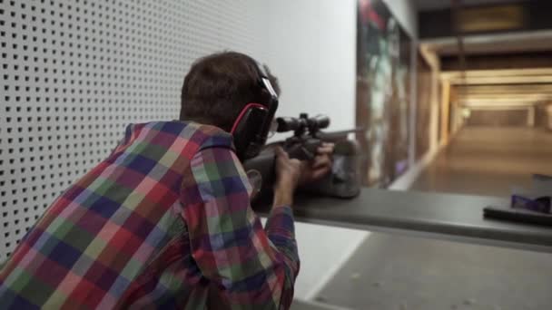 Rare view of a man shooting use a rifle at shooting range in headphones — Stock Video