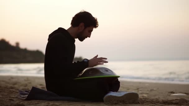 L'homme en noir occasionnel jouer accrocher assis sur la plage en face de la mer seul — Video